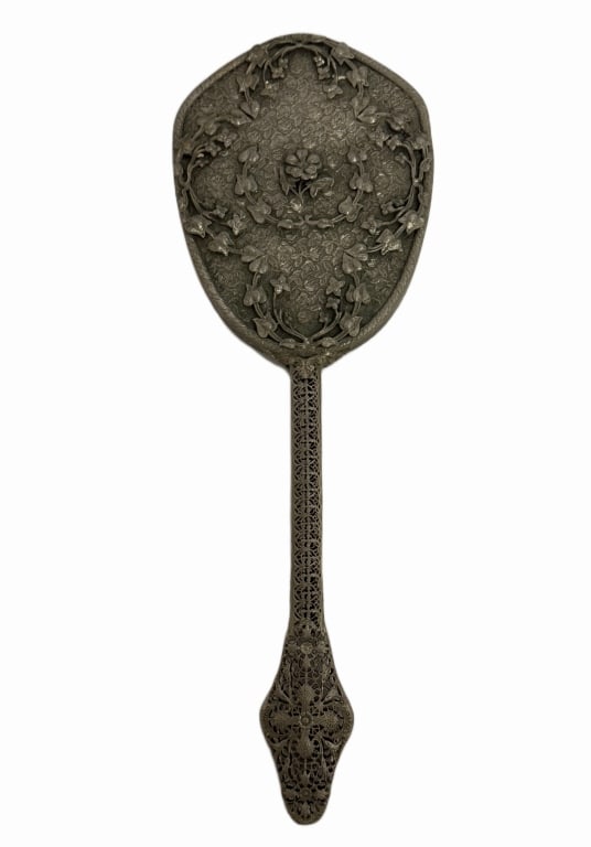Art Nouveau Botanical Filigree Vanity Hand Mirror: Item/Description: Antique vanity hand mirror featuring a shield-shaped back intricately overlaid with high-relief climbing ivy vines and a central blooming flower. Background is covered in a finely
