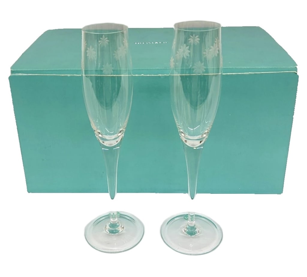 Tiffany & Co. "Magic" Crystal Champagne Flutes: Item/Description: A pair of contemporary clear crystal toasting flutes featuring tapered, elongated bowls meticulously wheel-engraved with a whimsical multi-sized starburst and daisy floral motif. The