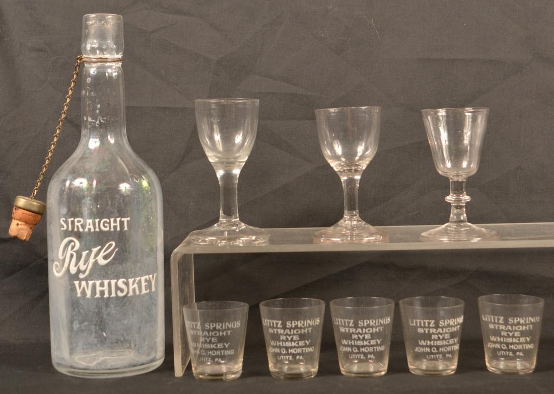 Nine Pieces of Antique Colorless Glass.: Nine Pieces of Antique Colorless Glass. "Straight Rye Whiskey" Bottle, five "Lititz Springs Straight Rye Whiskey, John C Horting, Lititz, PA" etched shot glasses, and three blown wines. Bottle measure