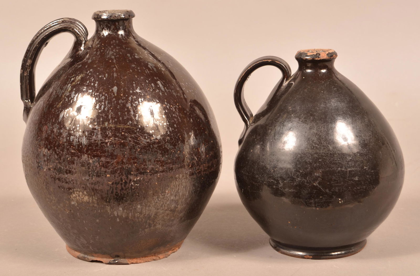 Two Ovoid Manganese Glazed Redware Jugs.: Two Ovoid Manganese Glazed Redware Jugs. Both with applied strap handles. 8-1/4" and 10"h. Condition: Good with chips and wear.