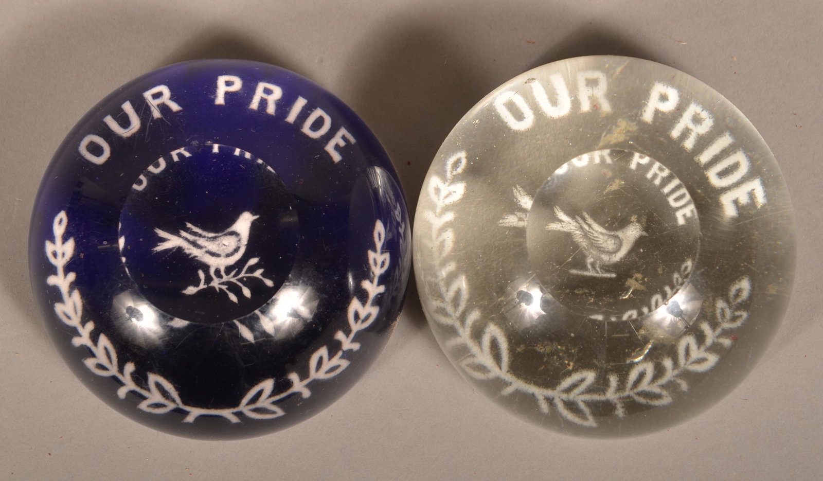 2 "Our Pride" Frit Paperweights with Dove and Garland.: Two "Our Pride" Frit Glass Paperweights with Dove and Garland. One cobalt and one colorless glass with top facets. Both 3-1/4'' diam. Condition: Good with wear and minor pin nips.