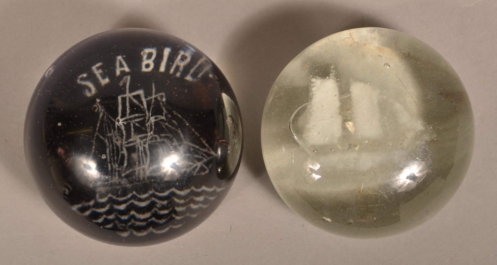 Two White Frit Oyster Schooner Paperweights.: Two White Frit Oyster Schooner Paperweights. "Sea Bird" on a cobalt blue ground, and one colorless glass. Both 3-1/2" diam. Condition: Good with wear.