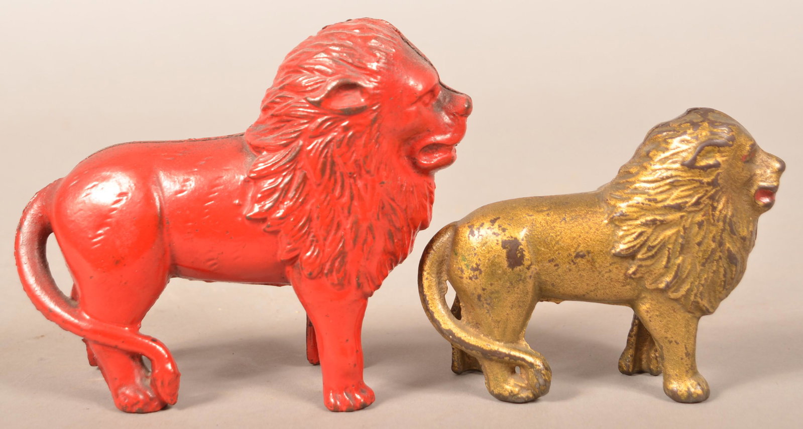 Two Arcade Lion with Tail Right Cast Iron Still Banks.: Two Arcade Ears Down Lion with Tail Right Cast Iron Still Banks. Painted gold, 4"h. and red, 5-1/4"h. Condition: Good with wear.