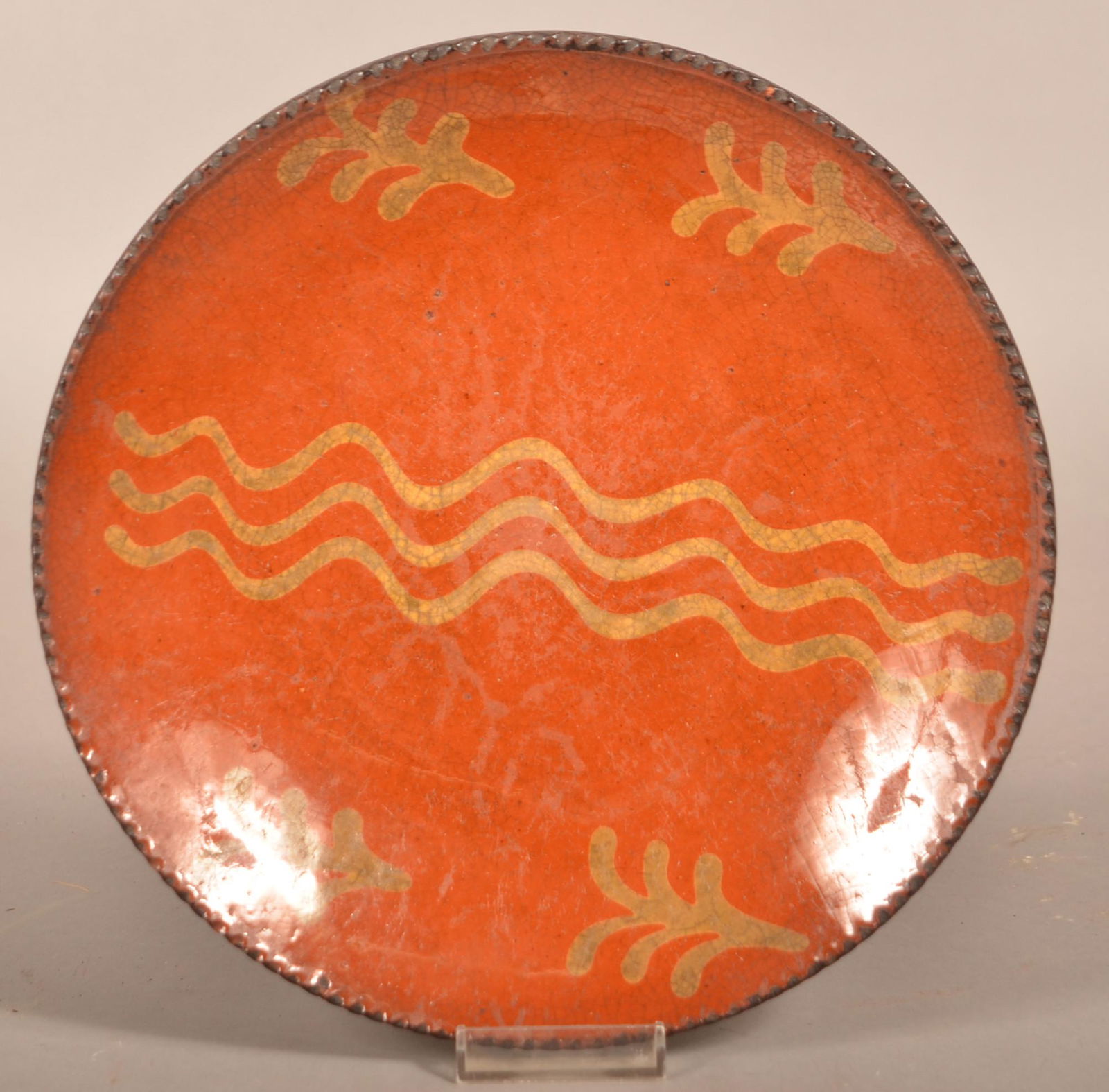 Pennsylvania Yellow Slip-Decorated Redware Plate.: Pennsylvania Yellow Slip-Decorated Redware Plate. 19th century. Coggle wheel edge with triple squiggle line slip-decoration in center flanked by four sprigs. 9-3/4" diam. Condition: Good with wear.