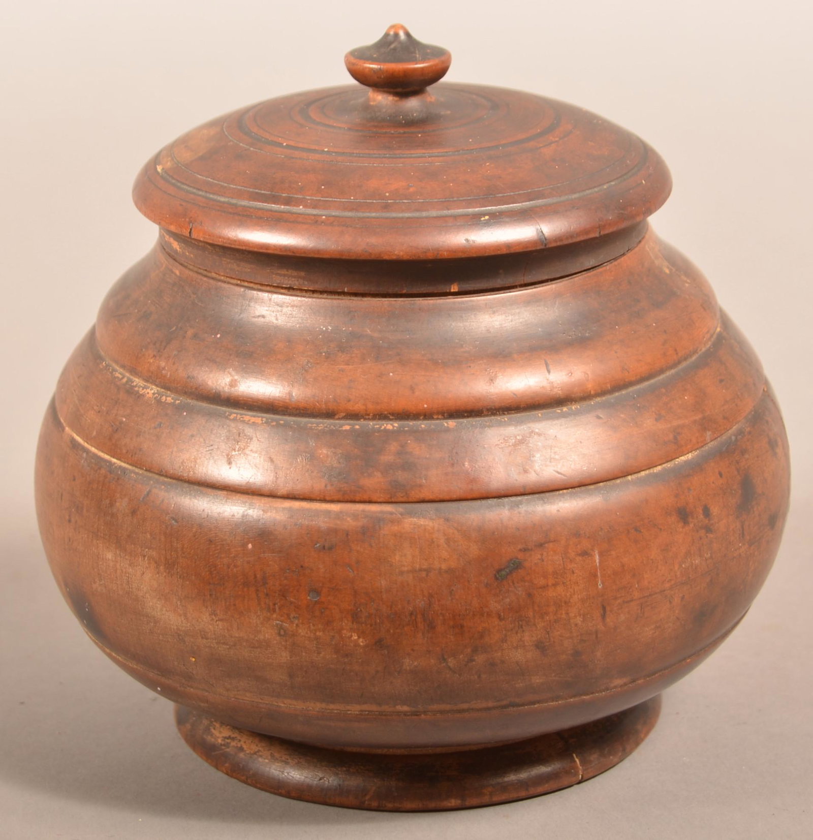 American 19th Century Treenware Covered Canister.: American 19th Century Treenware Covered Canister. Turned maple squat form with urn finial on dome lid and decorative ring turnings. 7"h. x 6-1/2" diam. Condition: Good with two age cracks.