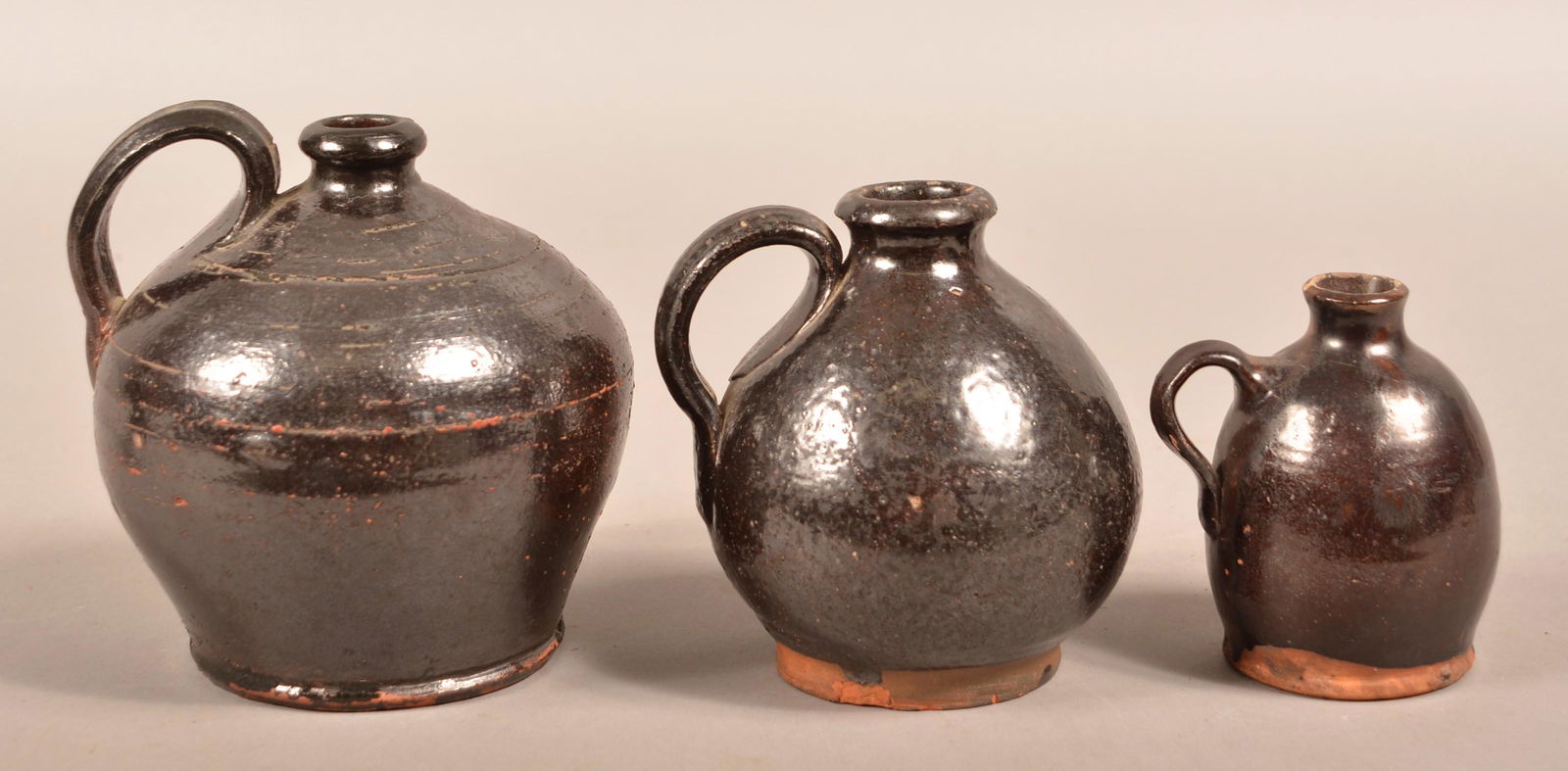 Three 19th Century Graduated Glazed Redware Jugs.: Three 19th Century Graduated Glazed Redware Jugs. Bulbous forms with applied loop handles. 4" to 6"h. Condition: Good with wear and minor chips.