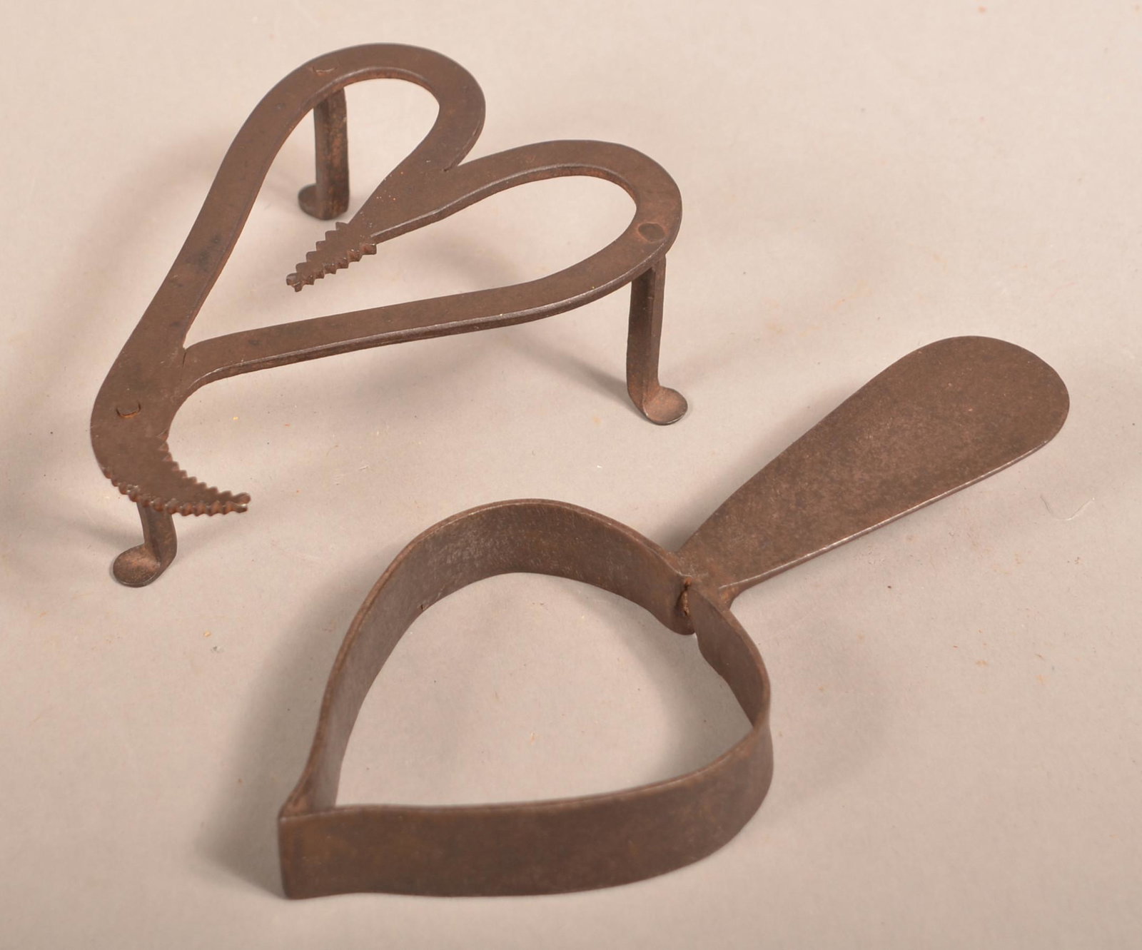 Two Early 19th Century Wrought Iron Trivets.: Two Early 19th Century Wrought Iron Trivets. Heart-form with sawtooth and scrolled end, 6"l. and a spade-form with flattened handle, 8"l. Condition: Good with pitting and rust.