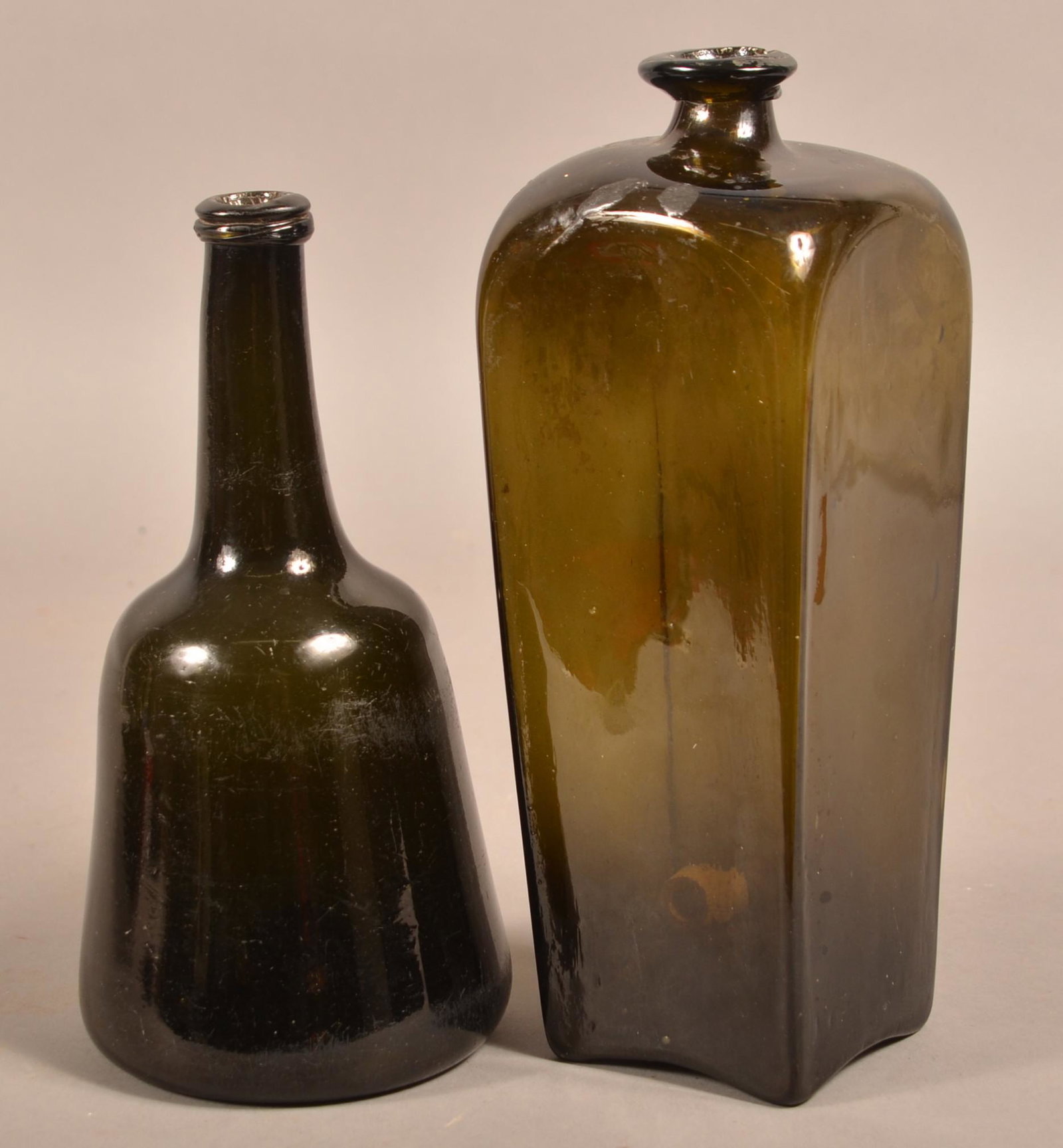 Two Early 19th Century Blown Olive Green Glass Bottles.: Two Early 19th Century Blown Olive Green Glass Bottles. Tapered side case bottle 10-1/4"h. and a funnel-shaped bottle with tapered elongated spout with applied mouth and concave base with pontil 9"h.