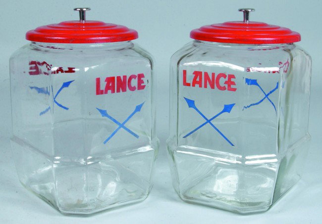 Two Colorless Glass Lance Cracker Canisters with o: Two Colorless Glass Lance Cracker Canisters with original deco lids with red and blue transfer "Lance" and crossed spears logo. 12" high. Condition: Good.