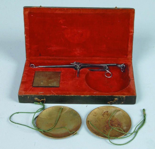 Cased Gold Scales, 3.25"w x 6.75"l.; steel balance: Cased Gold Scales, 3.25"w x 6.75"l.; steel balance beam with 2 string suspended 2.5"d. brass pans and 10 brass weights in a red velvet lined, tooled green leather covered wood box with hook and eye cl