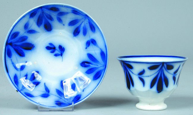 Flow Blue Ironstone Cup and Saucer, 3"h. x 6"d.; f: Flow Blue Ironstone Cup and Saucer, 3"h. x 6"d.; floral decorated handless twelve paneled cup with saucer. No marks. Condition: Tiny chip off rim of cup, o/w Good