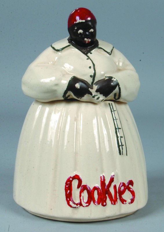 Black Memorabilia Cookie Jar, 11 1/4"h.; white cer: Black Memorabilia Cookie Jar, 11 1/4"h.; white ceramic Mammy type two part cookie jar, painted details. Signed: McCoy on bottom. Condition: five cracks from top of skirt on lower half, some paint loss
