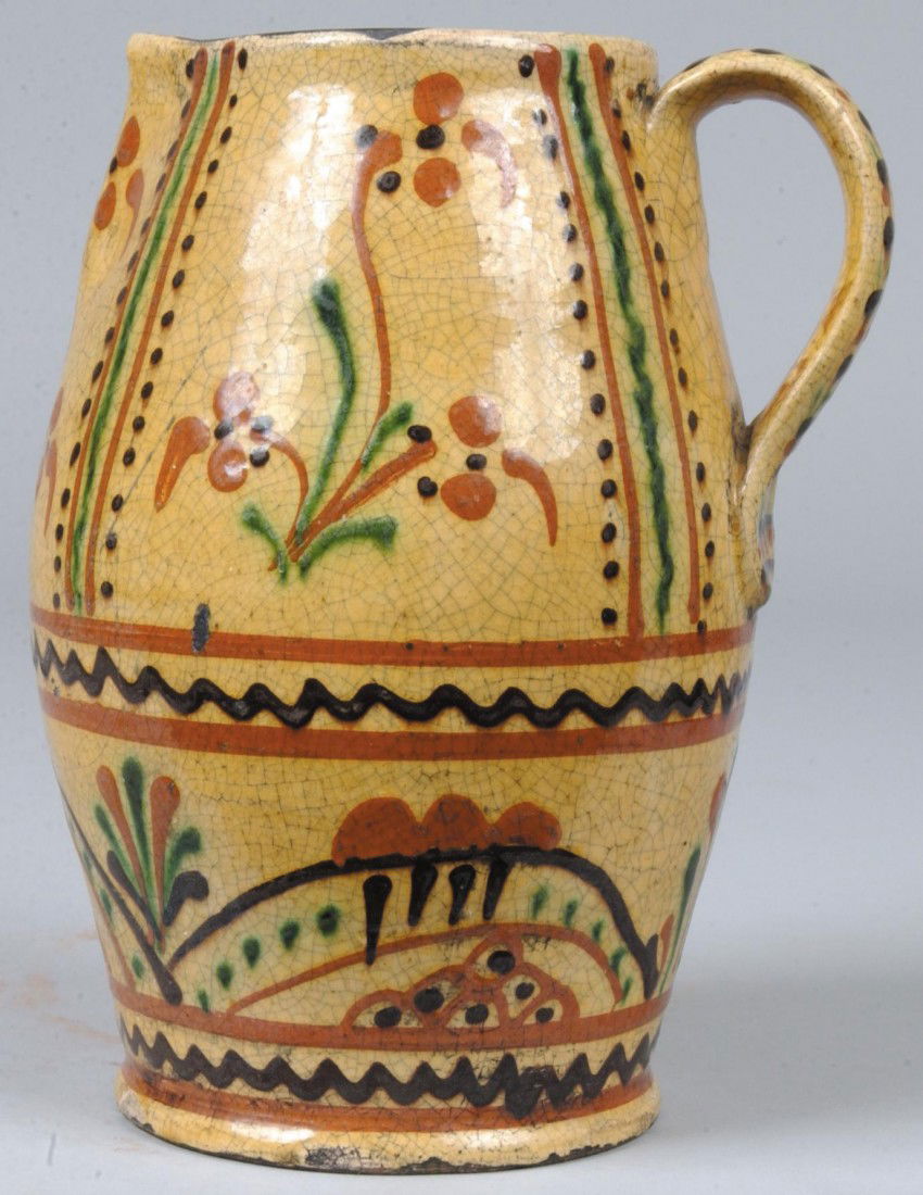 Shooner Marked Slip Decorated Redware Pitcher, appl: Shooner Marked Slip Decorated Redware Pitcher, applied strap handle, red, brown and green designs on yellow ground, marked: "Greg Shooner, 1998". 8 3/4"h. Condition: hole punched in bottom, chip on ba