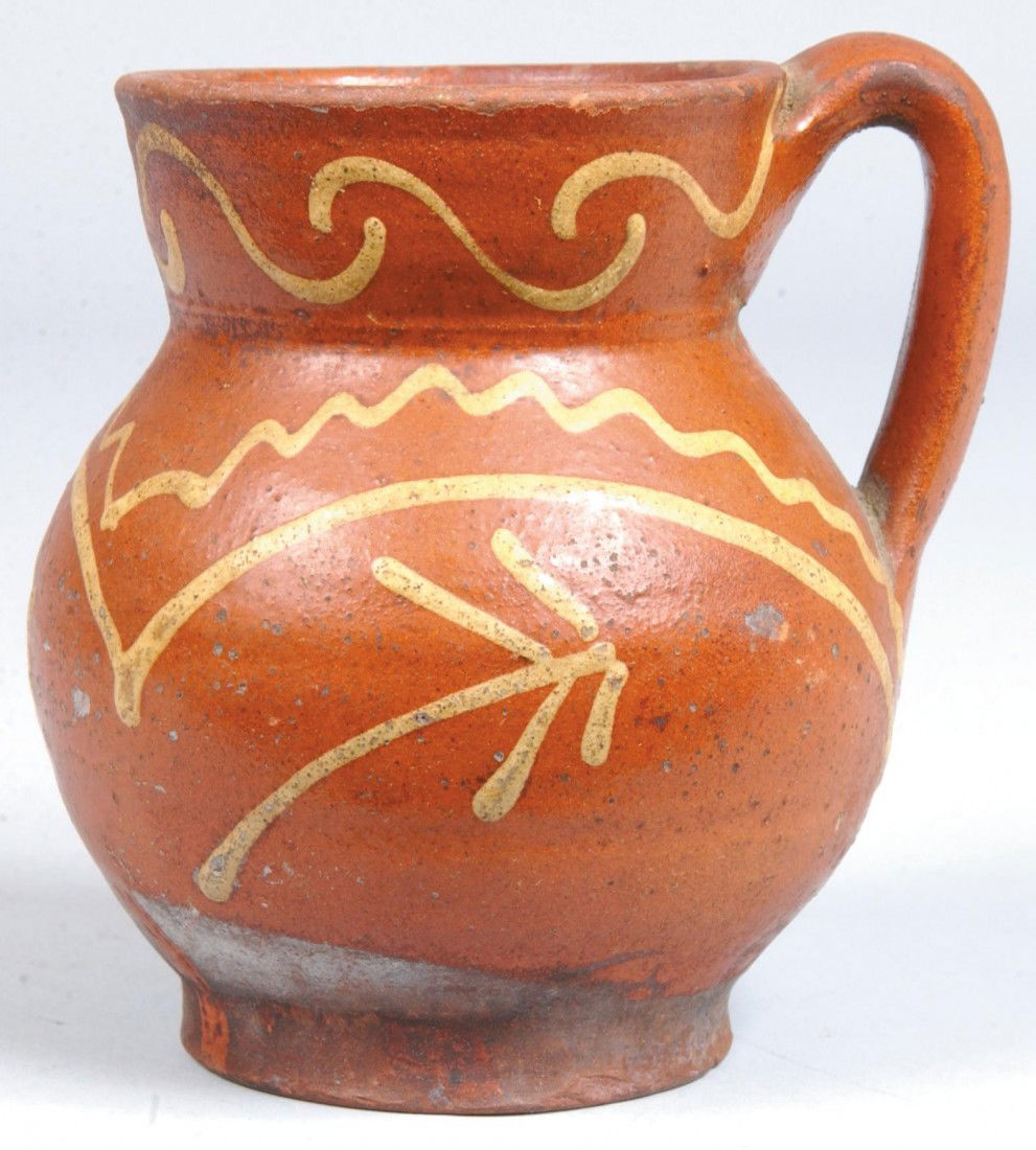 Redware Pitcher, applied loop handle, flared rim w: Redware Pitcher, applied loop handle, flared rim with raised foot, yellow slip line decoration. Unmarked. 5 1/4"h. Condition: two small chips at foot rim