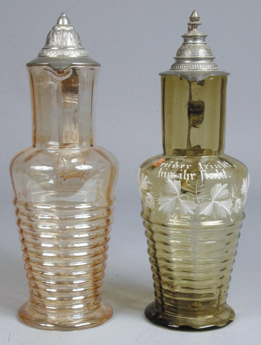 Two Blown Glass Flagon, one with iridescent finish: Two Blown Glass Flagon, one with iridescent finish, other olive green with hand enameled floral designs and phrase. Both with hinged pewter covers. No makers marks. 14 1/2"h. & 14 3/4"h. Condition: Go