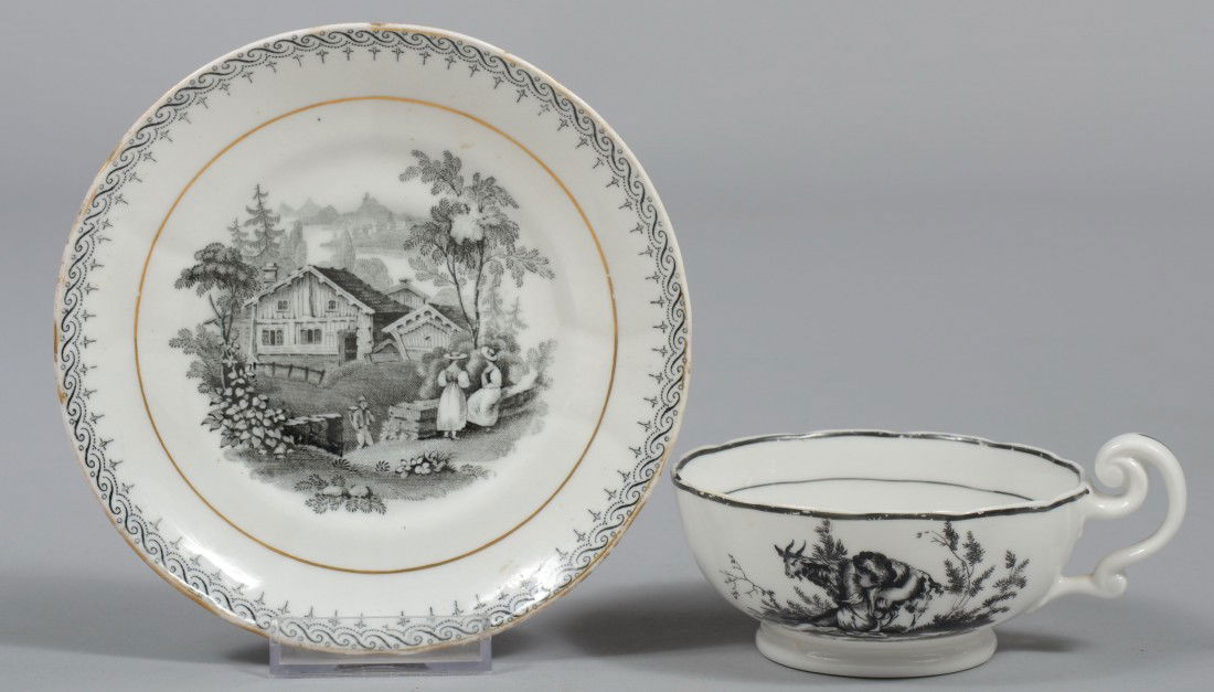 Black Transfer Cup and Saucer, country cottage and: Black Transfer Cup and Saucer, country cottage and children with animals. Marked: sun burst with number. 2"h. X 5 1/2"dia. Condition: Cup has chip inside rim