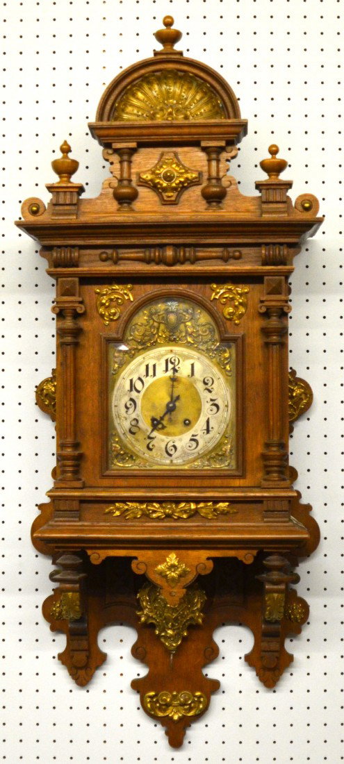 German Cased Pendulum Wall Clock. Spring driven wo: German Cased Pendulum Wall Clock. Spring driven works, maker unknown. Arched pediment with cast brass shell within, with three finials, assorted bosses and half turnings in wood and plated metal. Meta