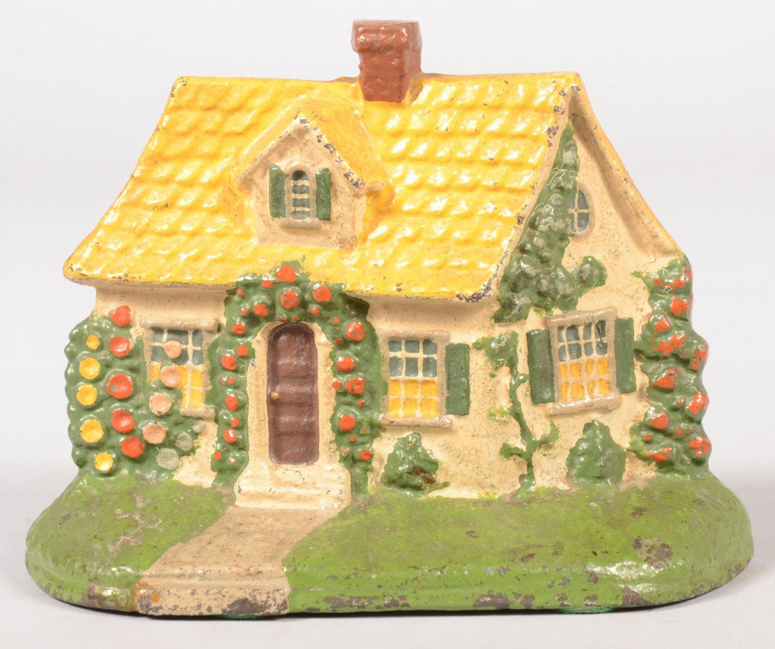 Hubley Cottage Doorstop. Flower and vine enrobed y: Hubley Cottage Doorstop. Flower and vine enrobed yellow roof cast iron cottage. 7"w. Condition: Good with use wear.