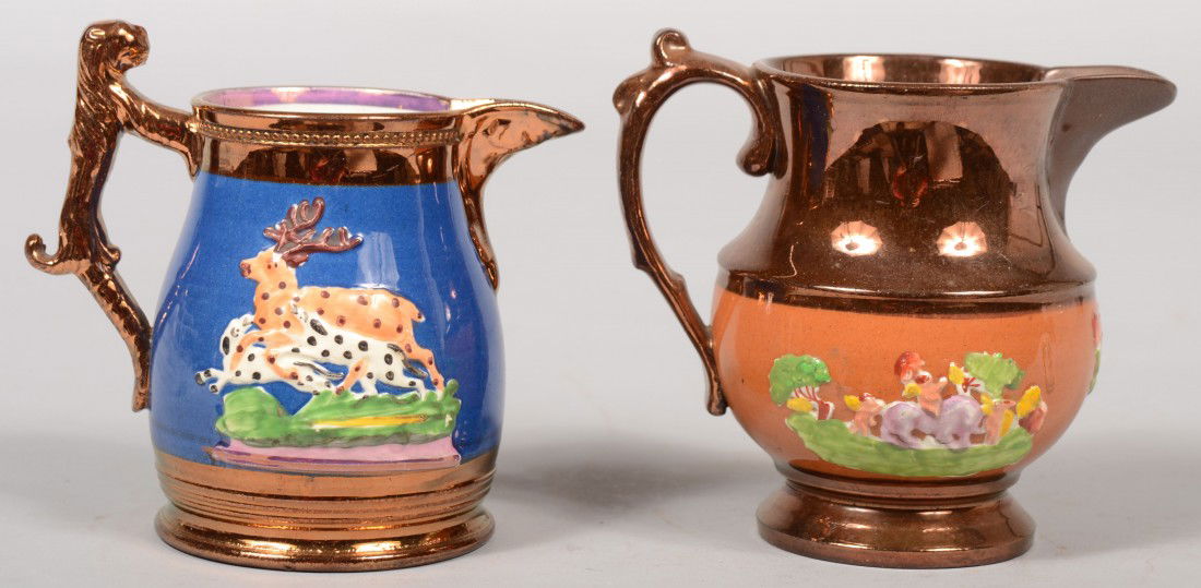 Two Copper Luster Pitchers. Adams style with raise: Two Copper Luster Pitchers. Adams style with raised foot, applied loop handle, pinch spout and burnt umber body band with applied vignettes of cherubs riding a lion. 5"h. X 3 3/4"dia. Other bulbous sh