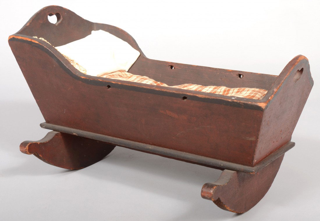 Dark Red Painted Wood Doll Cradle. Arched head and: Dark Red Painted Wood Doll Cradle. Arched head and foot boards with heart cut-outs. Crescent shaped rockers with ball ends. Painted accents in black. Accompanied by brown tabby mattress and lace trimm