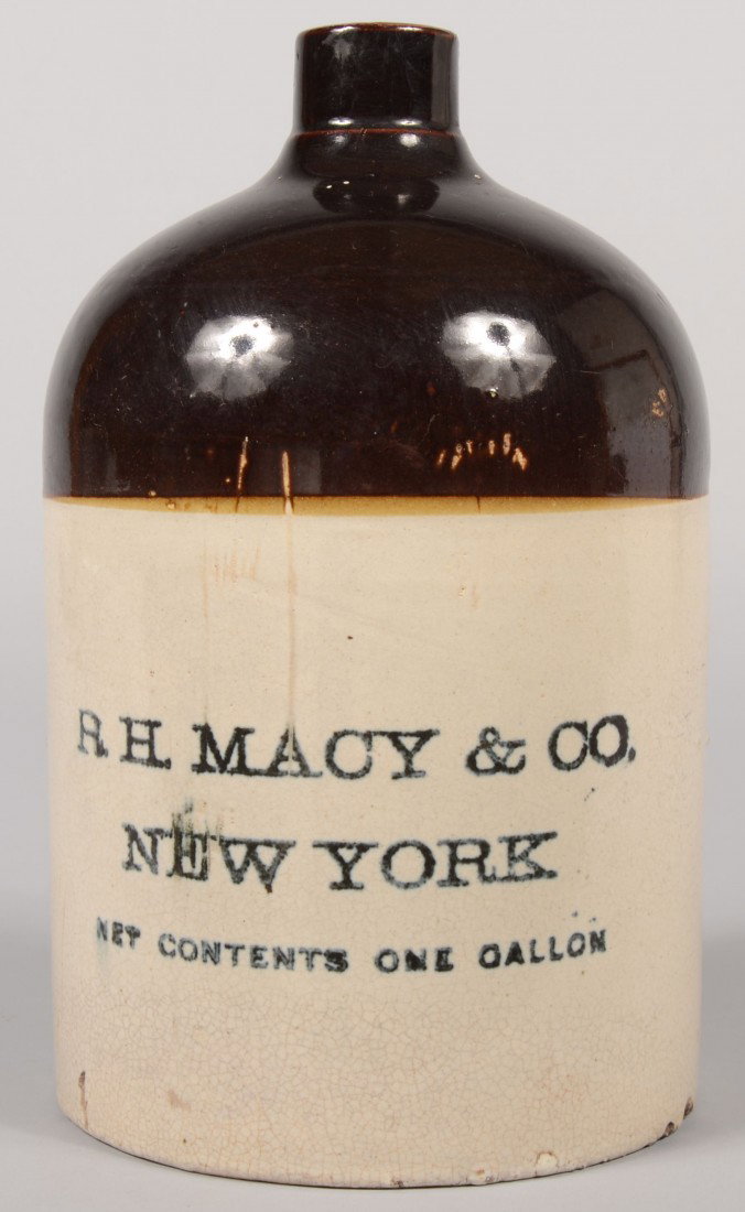 Stoneware Advertisement Jug. Top half dipped in man: Stoneware Advertisement Jug. Top half dipped in manganese. Printed cobalt label: "R. H. Macy & Co., New York. Net Contents One Gallon." Applied loop finger ring. 11"h. Condition: Two small chips off b