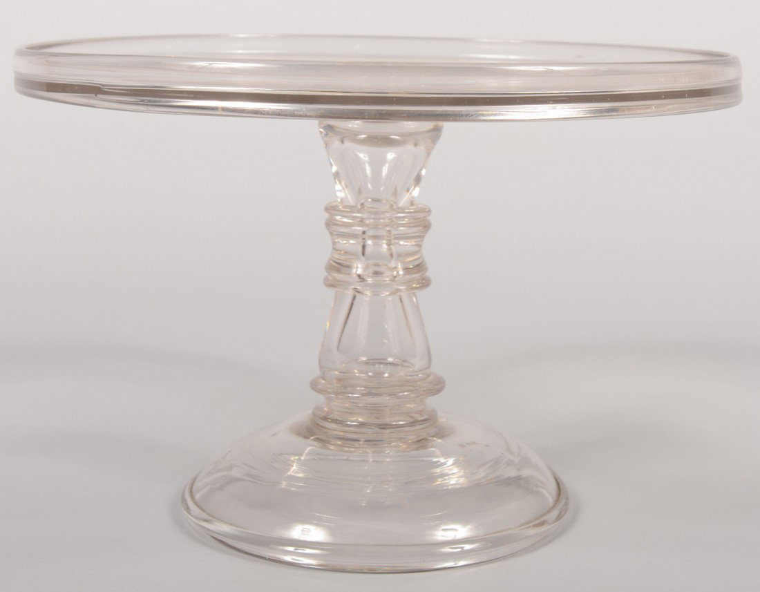 Blown Clear Flint Glass Cake Stand. Hollow ringed : Blown Clear Flint Glass Cake Stand. Hollow ringed hourglass shaped pedestal on domed base with rim bead. Flat circular table has a low galleried rim. 8 1/4"h. X 12 1/8"dia. Condition: Good, no damage.