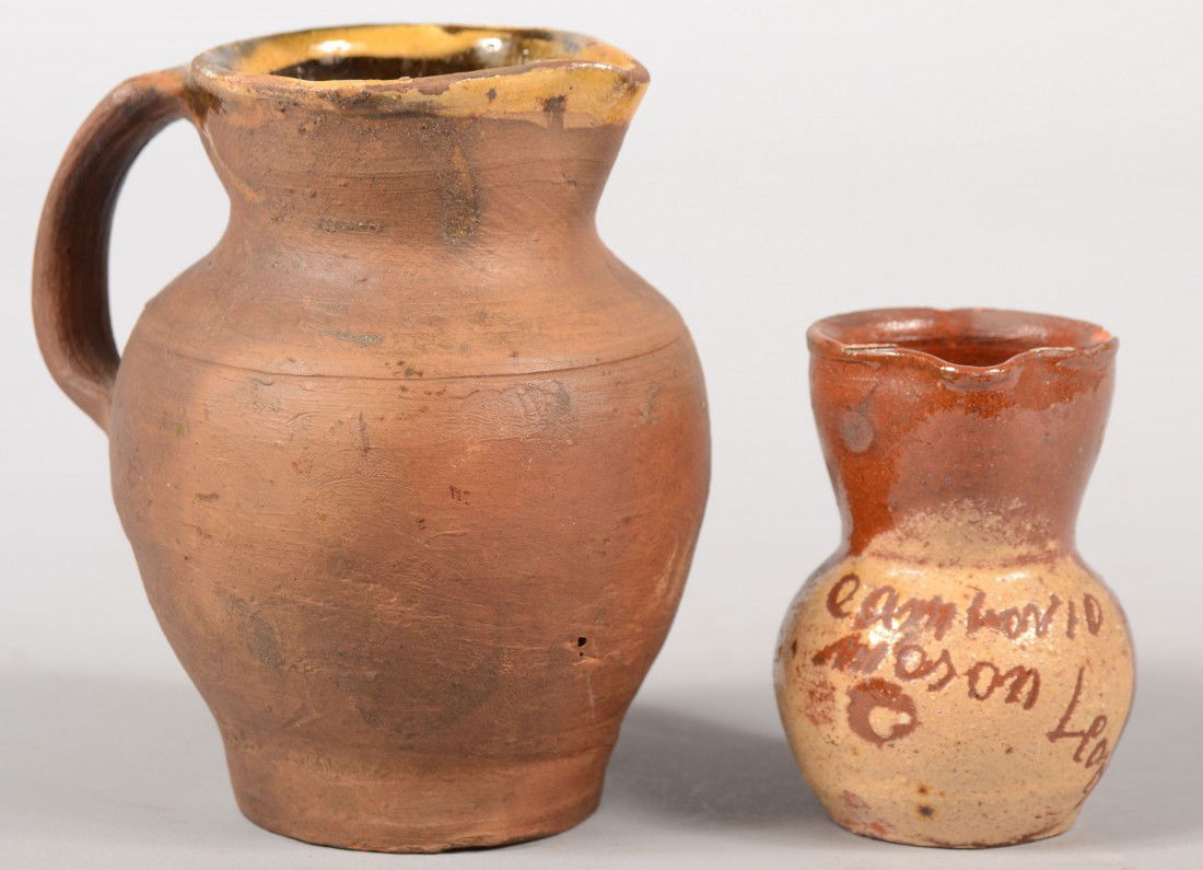 Two Small Earthenware Pitchers. A small redware p: Two Small Earthenware Pitchers. A small redware pitcher with a white glazed area on front with an inscription. 3"h. Along with tanware pitcher interior glazed, but not the exterior. 4 3/4"h. Condition