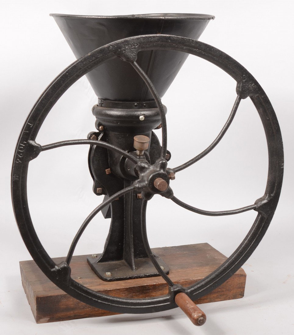 Large Cast Iron Meat Grinder. Mounted on a wood pl: Large Cast Iron Meat Grinder. Mounted on a wood plank. Unmarked. Having a conical sheet metal hopper and large flywheel with wood hand grip, but wheel is also grooved for a remote power source and bel