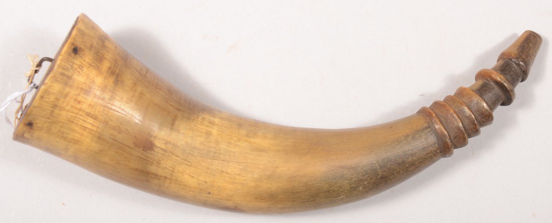 Powder horn measuring 10-3/4" along the outside cu: Powder horn measuring 10-3/4" along the outside curve having a 2-1/2" flat base plug and a raised carved spout with rings. Very good with the original iron staple in the base plug.