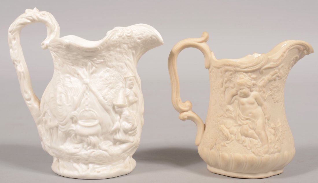Two White Parian Pitchers. Relief imagery on large: Two White Parian Pitchers. Relief imagery on larger of people camping in the woods and two women attending a campfire with kettle. Matte finish and molded loop handle. 5 1/2"h. Along with another pitc