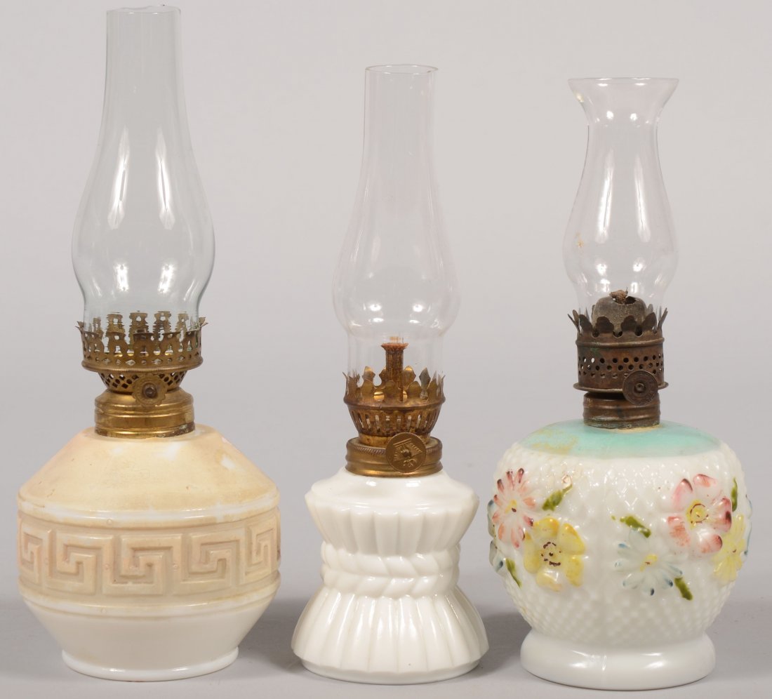 Three Milk Glass Font Bed Side Oil Lamps. Three di: Three Milk Glass Font Bed Side Oil Lamps. Three different press molded designs. One with surface painting to flowers. All with brass wick holders and colorless glass chimneys. 3 3/4"h., 3 1/2"h. and 3