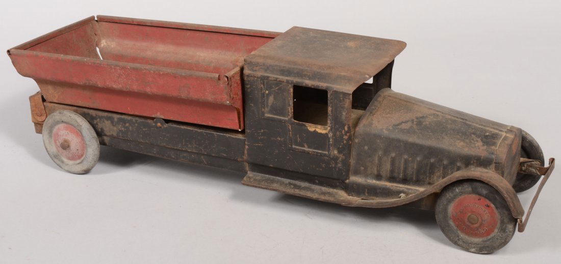 Cor-Cor Pressed Steel Dump Truck. Black body and c: Cor-Cor Pressed Steel Dump Truck. Black body and chassis with a red dump bed and four pressed composite wheels with red hubs marked: "Cor-Cor, Washington, Ind." 6 1/2"h. X 22 1/4"l. X 6 3/8"w.