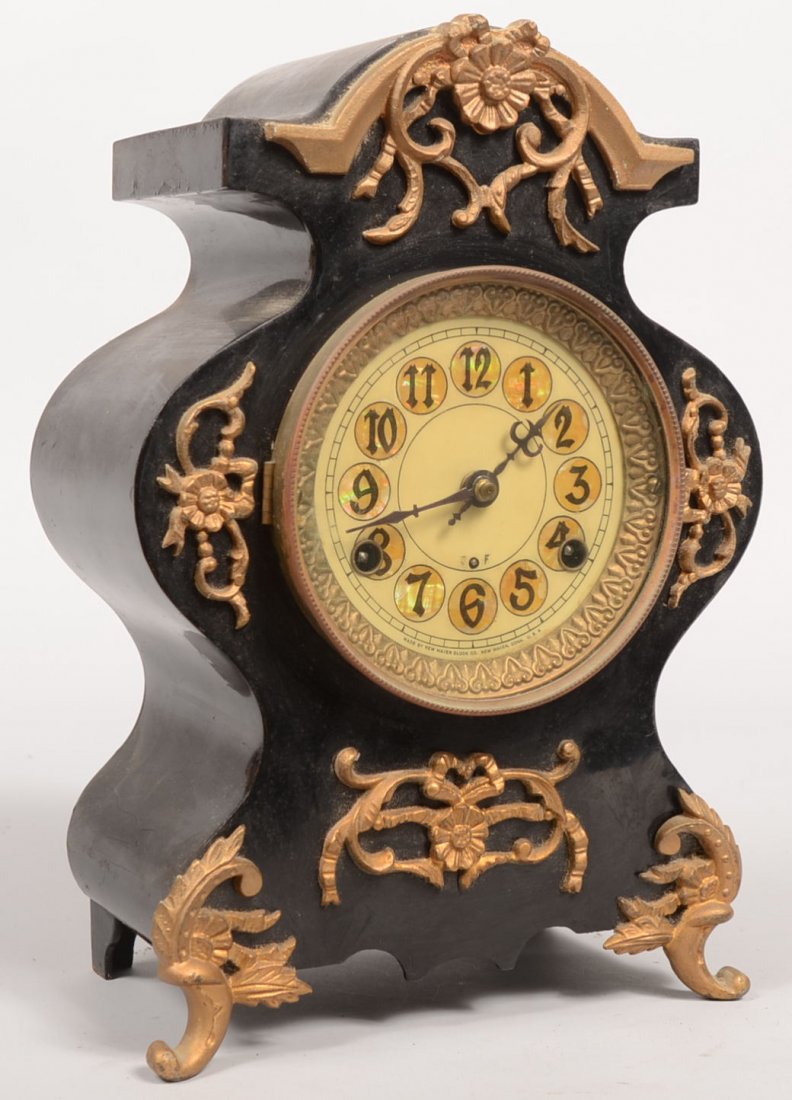 A Steel Cased New Haven Mantle Clock. Black steel c: A Steel Cased New Haven Mantle Clock. Black steel case has applied cast brass ormolu and hinged bezel with glass lens. White enameled chapter ring has mother of pearl number discs. All brass works ins