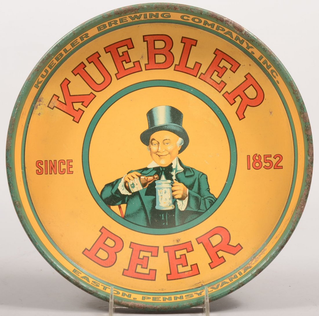 Lithographed Steel Beer Tray. Round tray with "Kue: Lithographed Steel Beer Tray. Round tray with "Kuebler Beer", Since 1852, Easton, PA. Showing a top hatted gentleman pouring a beer. 1 1/2"h. X 12"dia. Condition: Good with use wear. Some rust on rim.