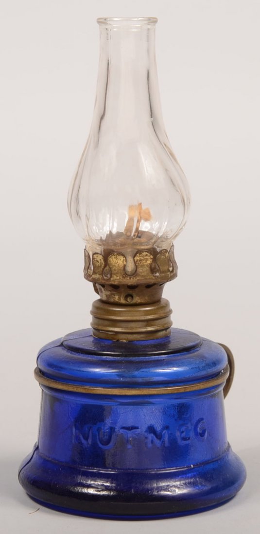 Blue Glass "Nutmeg" Finger Ring Oil Lamp. Cylindri: Blue Glass "Nutmeg" Finger Ring Oil Lamp. Cylindrical base font with a clip-on brass wire finger ring. Applied brass collar and threaded brass burner with twisted optic colorless chimney. 6 1/4"h. Con