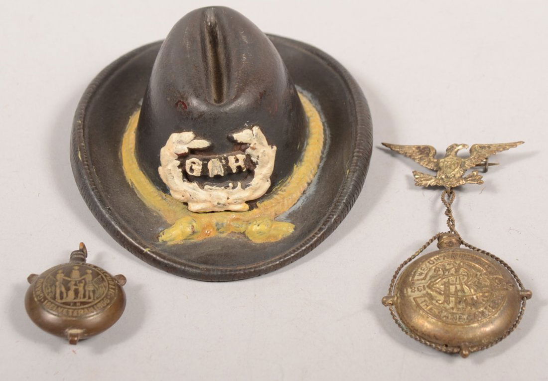 Three GAR Souvenirs. A cast iron campaign hat asht: Three GAR Souvenirs. A cast iron campaign hat ashtray in blue with gold hat cord and white wreath with GAR on crown. 1 1/2"h. X 4"l. A silver plated brass canteen with twisted wire strap hanging from