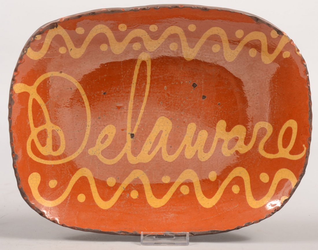 Greg Shooner Delaware Marked Redware Loaf Dish. Cogg: Greg Shooner Delaware Marked Redware Loaf Dish. Coggle rimmed oblong dish has yellow slip wavy lines with dots at top and bottom borders with Delaware in cursive through the middle. Back has signature
