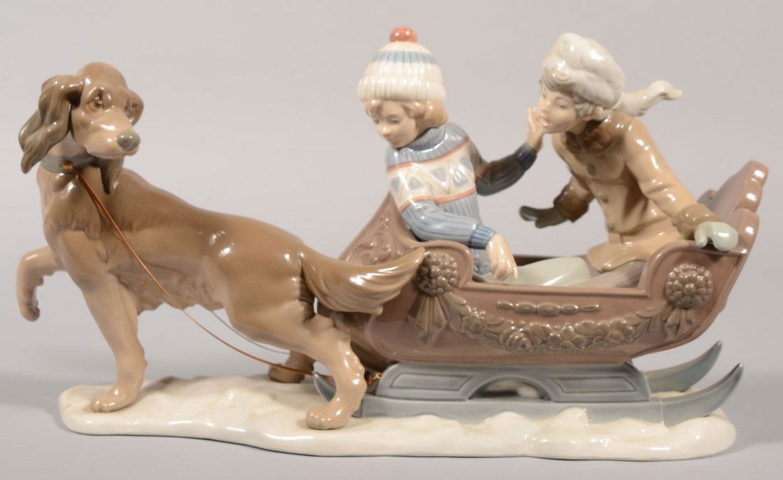 Lladro Cast Sculpture "Sleigh Ride." Model 2349M.: Lladro Cast Sculpture "Sleigh Ride." Model 2349M. Boy and girl in winter garb in a cutter being pulled by a reluctant brown dog. Setting on an oblong snow covered base. Dog has leather rein attached t