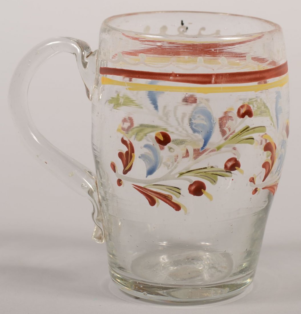 Paint Decorated Stiegel Type Handled Glass Mug. Ba: Paint Decorated Stiegel Type Handled Glass Mug. Barrel shaped colorless glass body has applied loop handle with crimped terminus. Floral sprays in green, blue, white, yellow and red. Broken pontil. 4"