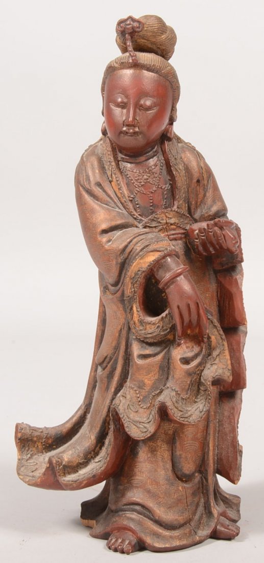 Carved and Paint Decorated Buddhist Figure. Figure: Carved and Paint Decorated Buddhist Figure. Figure is dressed in swaddling gown and is holding a small bag or purse. Reddish brown stain over a gold paint with designs drawn through the stain. 11 1/2"