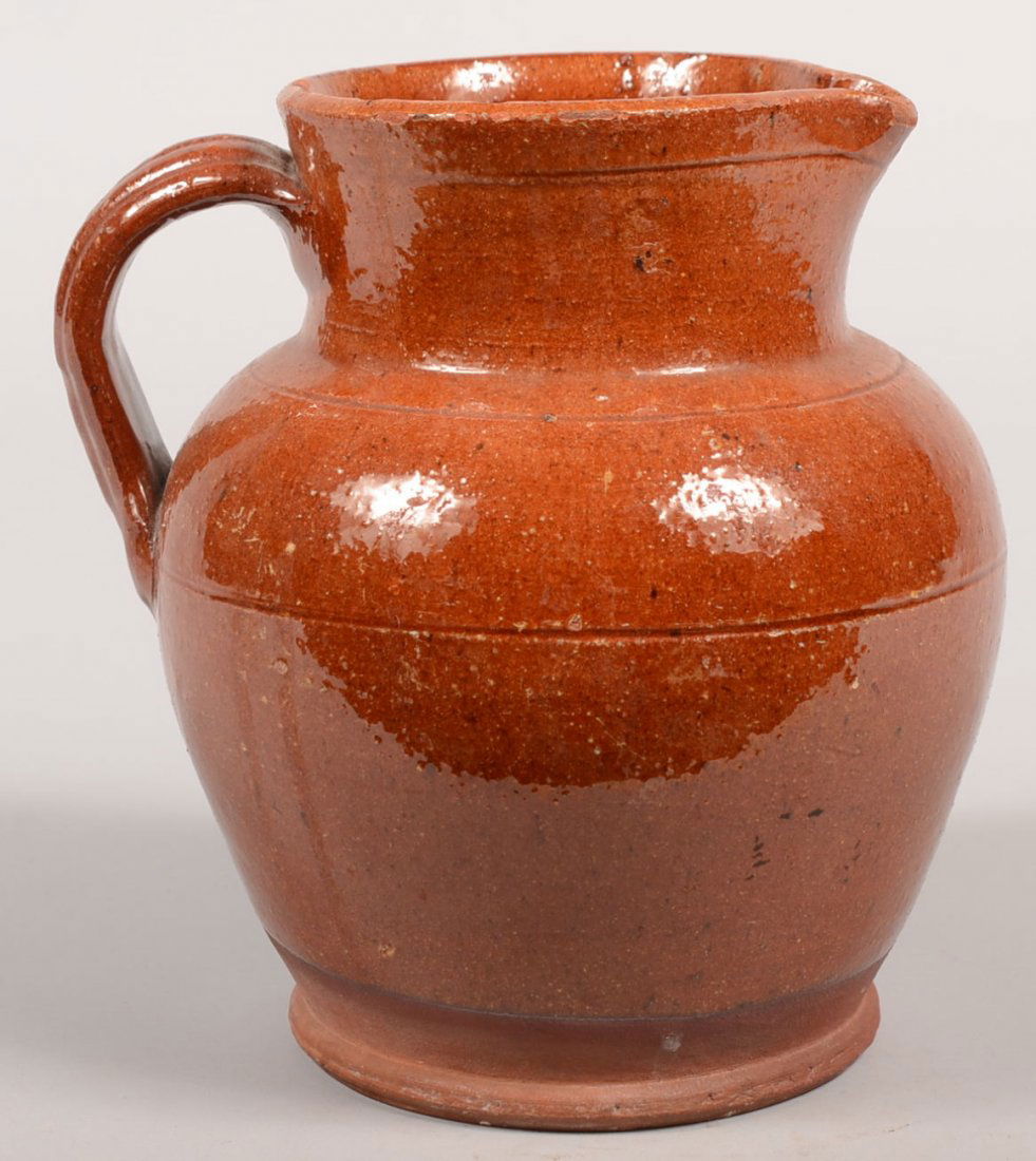 Redware Pitcher. Wide low body with high collar ha: Redware Pitcher. Wide low body with high collar having an applied reeded loop handle and a pulled spout. Glaze extends to within an inch of the beaded base. 7 5/8"h. X 6 3/4"dia.