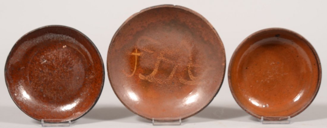 Three Salt Glazed Redware Dishes. Largest has free: Three Salt Glazed Redware Dishes. Largest has free-hand yellow slip decoration in center with incomplete glazing. 8 3/8"dia. Other two plain with glazed interior. 7"dia. and 6 1/2"dia.