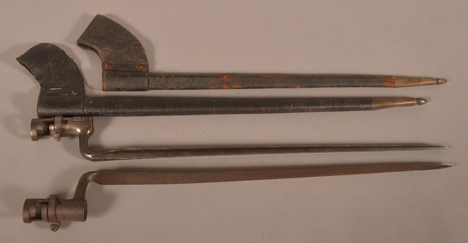 2 mod. 1855 Socket Bayonets: Includes dry, age-cracked leather scabbards with brass fittings. One bayonet has excessive finish wear and pitting with a visible Letter "U" proof mark. The other bayonet has no visible markings and h
