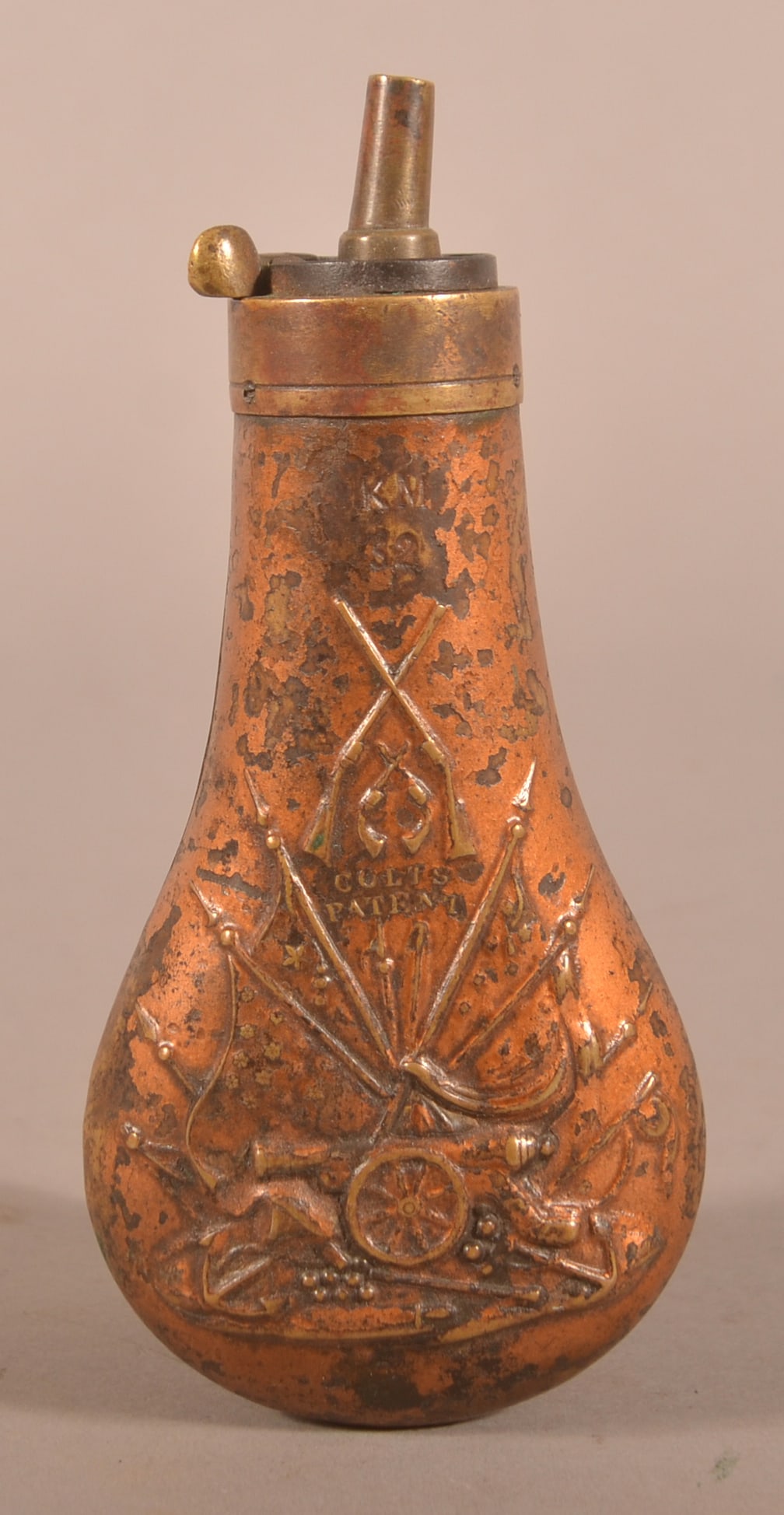Colt "Kreigsmarine" Powder Flask: "KM" marking on the top of the flask by the spout, flask has had a later-applied finish that is flaking off and is wearing away exposing the brass underneath, clear embossing featuring a late pattern