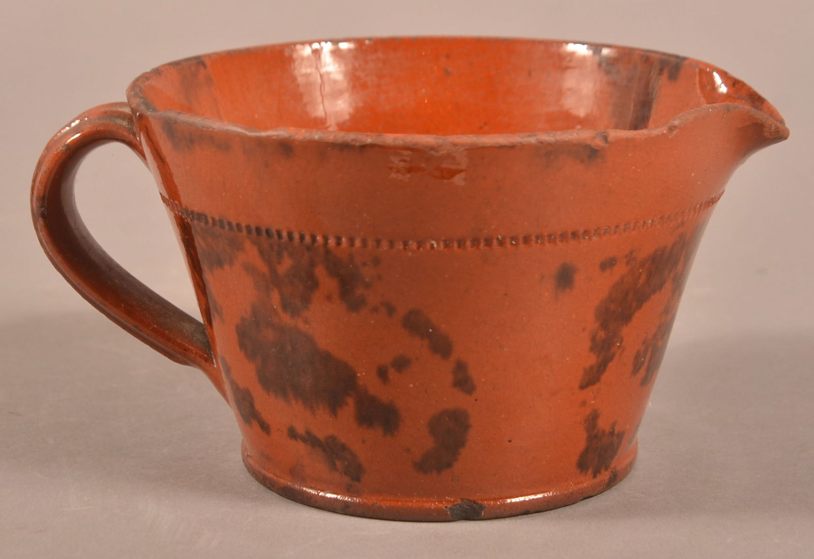 PA 19th C. Mottled Glaze Redware Pitcher.: Pennsylvania 19th Century Mottled Glaze Redware Pitcher. Squat form with tapered sides, applied molded loop handle and coggle-wheel incised shoulder. 3"h.
