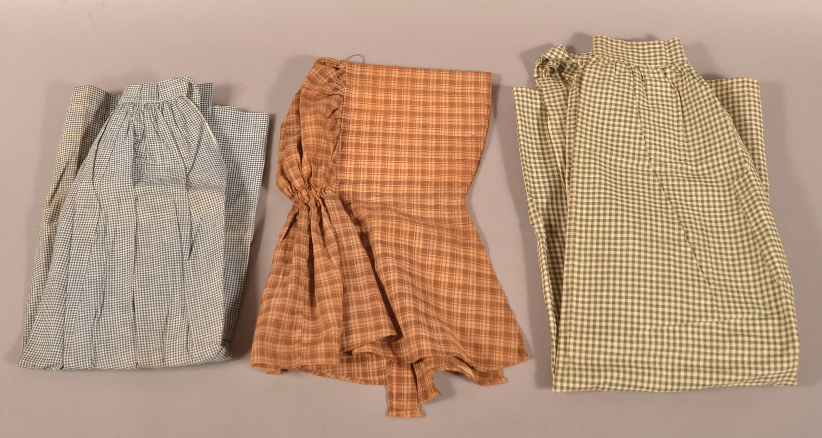 Three 19th Century Fabric Clothing Items.: Three 19th Century Fabric Clothing Items. Including a checked brown bonnet, 17"h., checked blue apron, 28"l. and a checked green apron with a pocket, 40"l.
