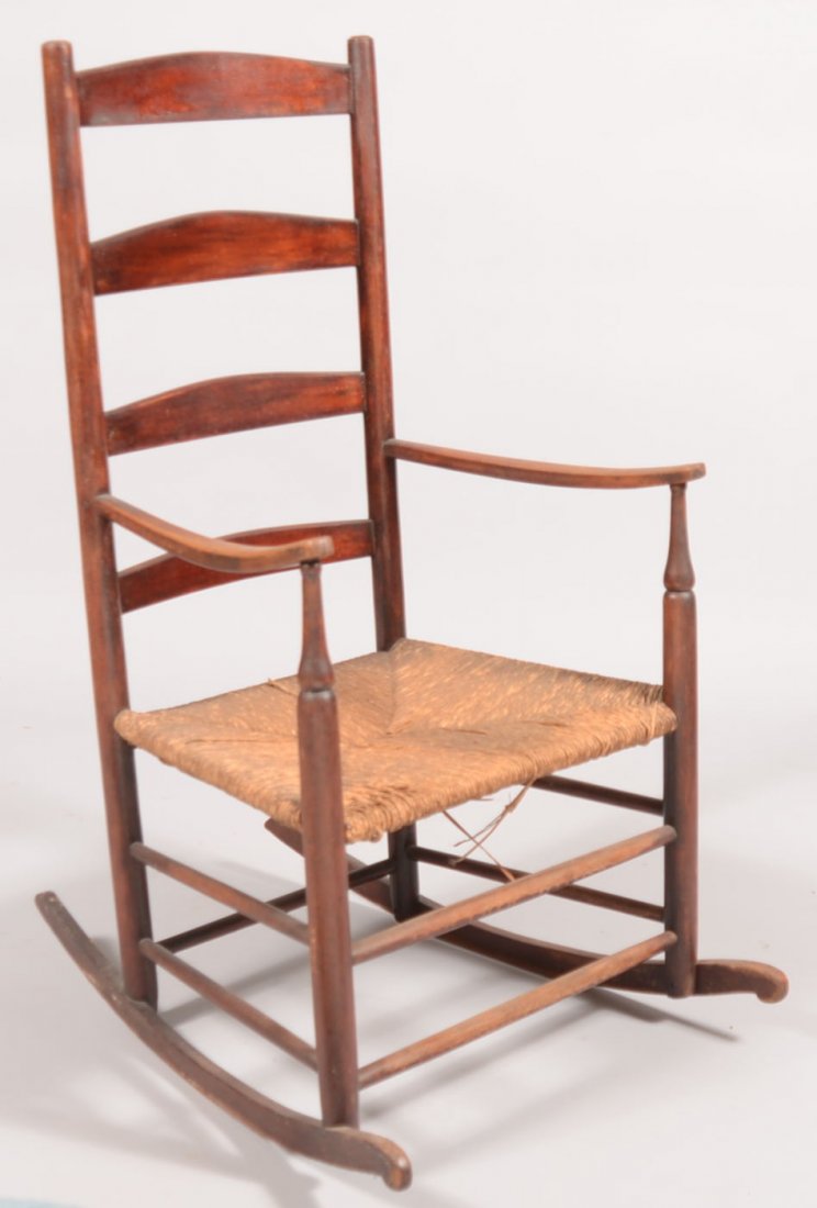 Dark Stained Ladderback Rocking Armchair. Four curved t: Dark Stained Ladderback Rocking Armchair. Four curved top back slats on round posts, up curved arms on vasiform front posts, rush seat, tapered dowel stretchers and flat carved rockers. 44"h. X 24 1/2