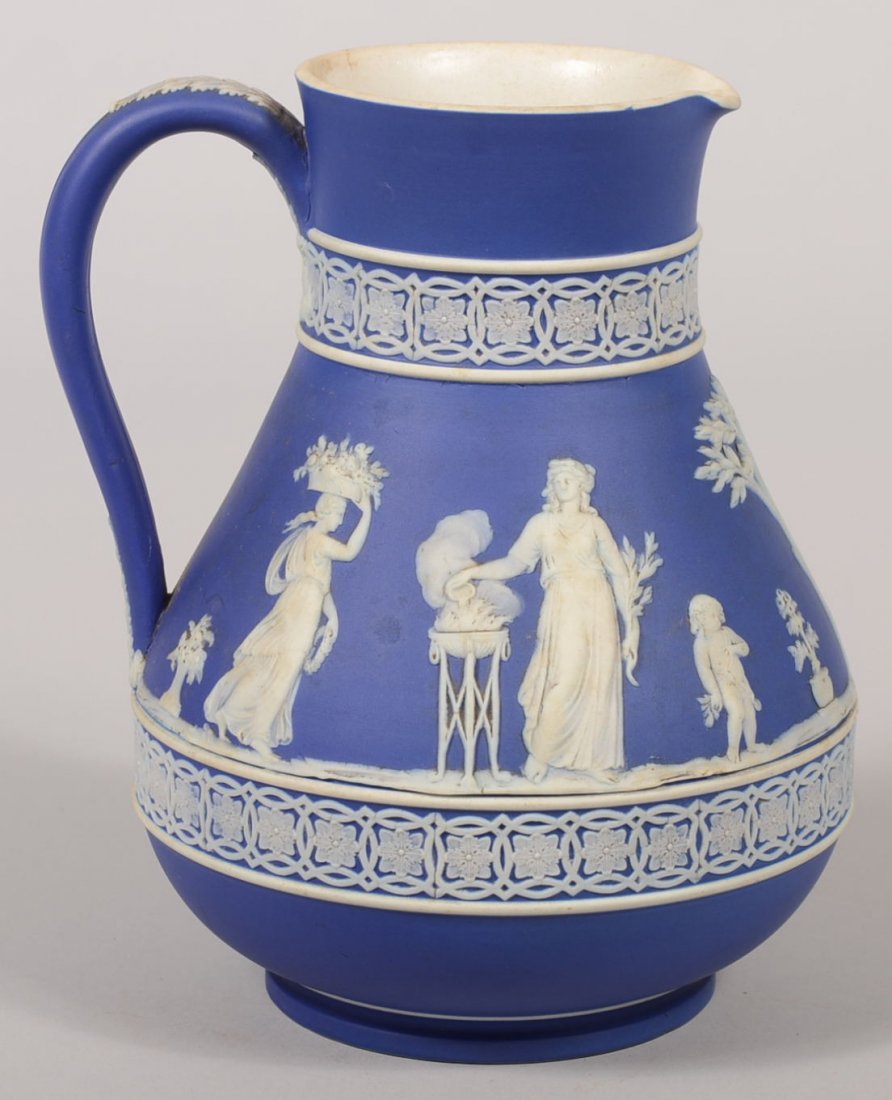 Blue Wedgwood Jasperware Pitcher. Bulbous vessel has ra: Blue Wedgwood Jasperware Pitcher. Bulbous vessel has raised white Classical Greek female figures with tree and putti on lower body and a floral border on neck and at base of bulb above a short foot. A
