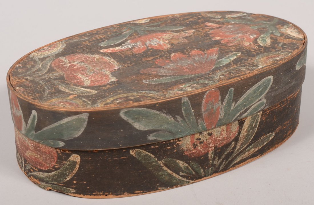 Painted Wood "Bucher" Band Box. Oval box with banded li: Painted Wood "Bucher" Band Box. Oval box with banded lid has black ground with red, white and blue flowers throughout. 3 1/2"h. X 11 3/4"l. X 7 1/4"w. Condition: Lid has a replaced band to edge. Chip 