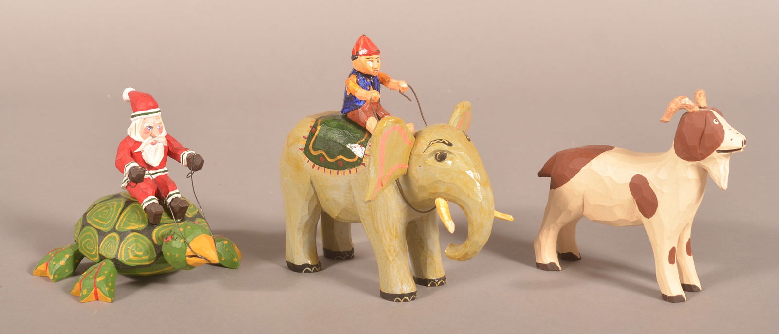 Three J. Bastian Folk Art Animal Carvings.: Santa riding a turtle, man riding an elephant, and a goat. 4-1/2" H to 6" H
